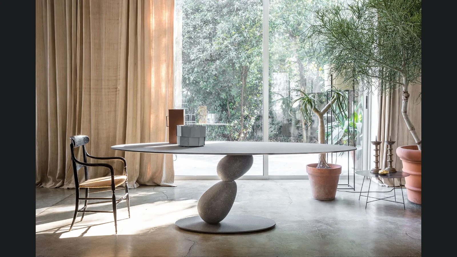 Tavolo ovale con struttura in metallo e piano in MDF rivestito con finiture materiche con due sassi che sorreggono il piano Matera di Mogg